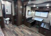 Interior of a modern camper/RV living space with dark wood cabinets, a booth dinette, and a large window with blinds.