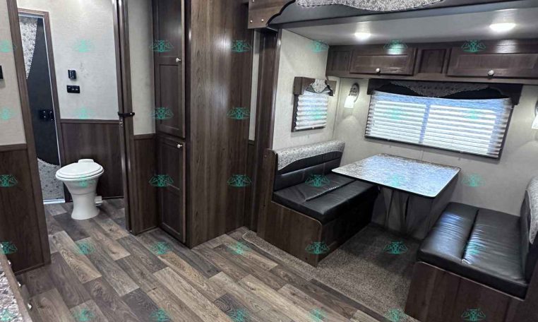 Interior of a modern camper/RV living space with dark wood cabinets, a booth dinette, and a large window with blinds.