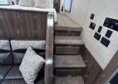Interior of a compact trailer with a loft bed, gray cushions, and dark wood cabinets above a sofa area.