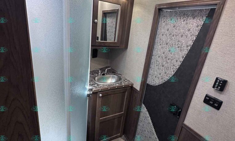RV bathroom with curved glass shower, dark wood vanity and mirror, small toilet, and textured door panel.