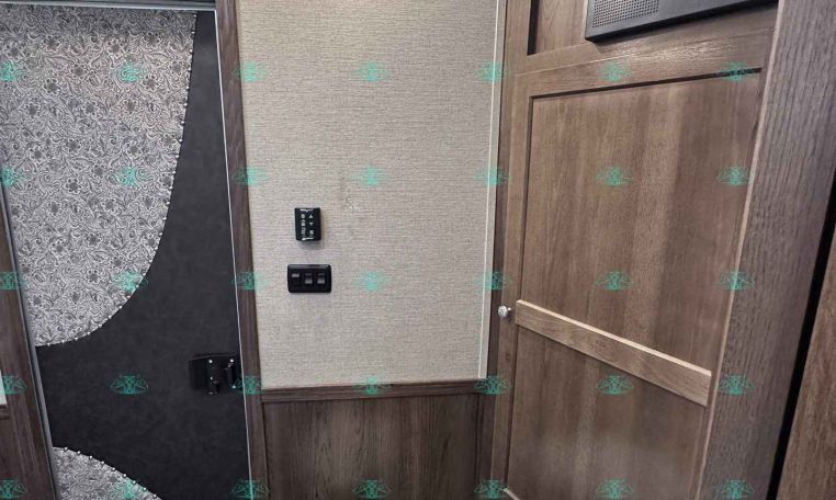 RV bathroom with wood-paneled walls, white toilet in foreground, and a curved glass shower with patterned curtain on the left; skylight above.