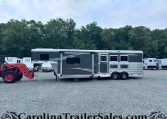 Silver and gray horse trailer on a gravel lot, with a red tractor in the foreground and several trailers beside it, trees and a blue sky in the background. Bottom edge shows decorative text reading CarolinaTrailersSales.com.