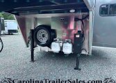 Open storage compartment of a trailer showing a spare tire, propane tanks, and a metal toolbox with cables and hoses inside a metallic enclosure.