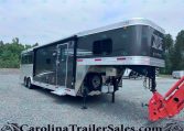 Large dark gray gooseneck horse trailer with living quarters, parked on a gravel lot with a side door and windows visible, propane tanks beneath.”