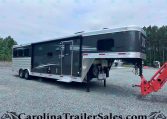 Dark gray fifth-wheel horse trailer on a gravel lot with front jacks down and towing equipment nearby, trees in the background.