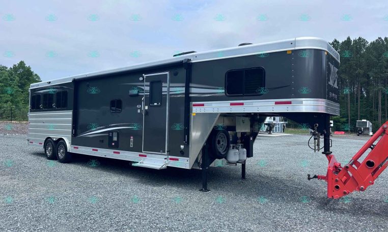 Dark gray fifth-wheel horse trailer on a gravel lot with front jacks down and towing equipment nearby, trees in the background.