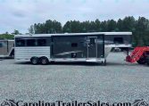 Side view of a black and silver Merhow horse trailer with living quarters, parked on a gravel lot with trees behind.