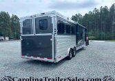 Silver-and-black Merhow horse trailer parked on a gravel lot with a forest backdrop; rear and side doors visible.