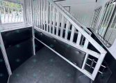 Interior of a silver horse trailer with a metal slatted divider, stepping ramp, and side windows