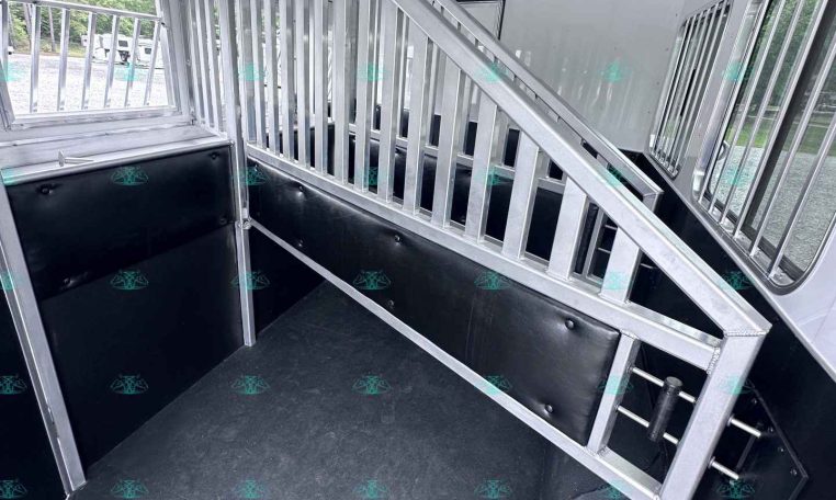 Interior of a silver horse trailer with a metal slatted divider, stepping ramp, and side windows