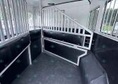 Interior of a horse trailer with metal stall dividers, padded walls, and a textured rubber floor area.