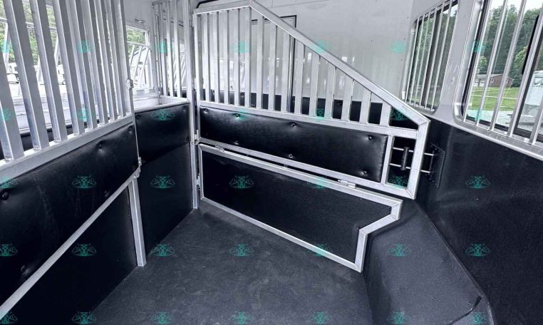Interior of a horse trailer with metal stall dividers, padded walls, and a textured rubber floor area.