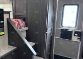 Interior of a dark wood-trimmed trailer showing stairs with a fabric blanket, cabinet storage, and an entry door with a window.