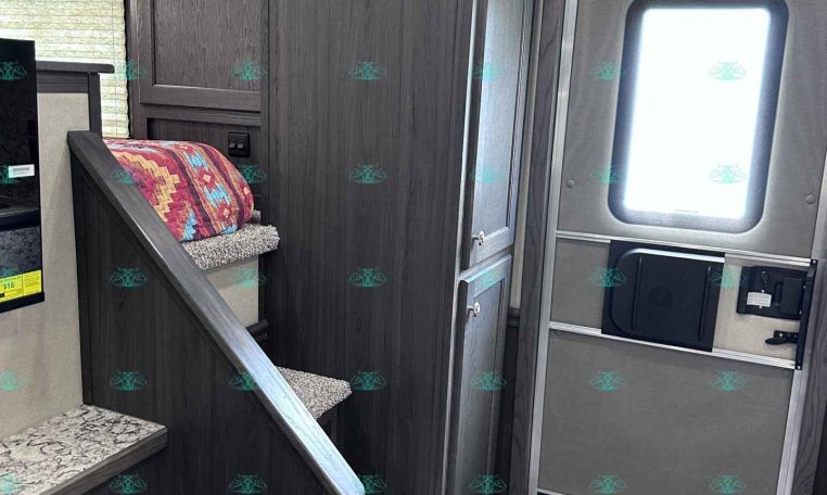 Interior of a dark wood-trimmed trailer showing stairs with a fabric blanket, cabinet storage, and an entry door with a window.