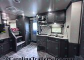 Modern RV kitchen with dark wood cabinets, stainless microwave, double sink, and marble-like backsplash.