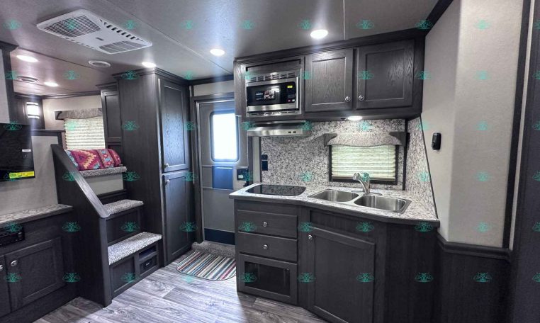 Modern RV kitchen with dark wood cabinets, stainless microwave, double sink, and marble-like backsplash.