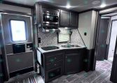 Compact RV kitchen with dark cabinets, stainless steel microwave, and dual-basin sink against a granite backsplash.