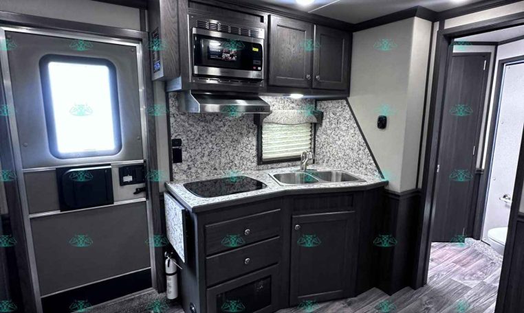 Compact RV kitchen with dark cabinets, stainless steel microwave, and dual-basin sink against a granite backsplash.