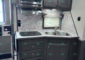 Compact RV kitchen with dark wood cabinets, stainless microwave, and a double sink on a marble-pattern counter.