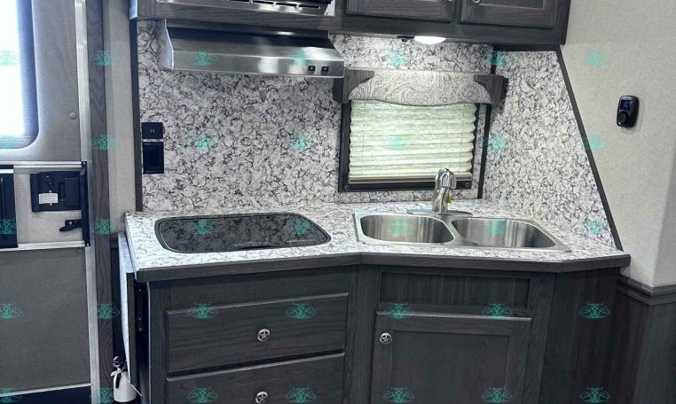 Compact RV kitchen with dark wood cabinets, stainless microwave, and a double sink on a marble-pattern counter.