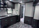 Modern RV kitchen with dark wood cabinets, stainless microwave, double sink, and granite-like countertops.
