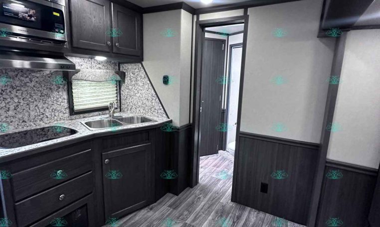 Modern RV kitchen with dark wood cabinets, stainless microwave, double sink, and granite-like countertops.