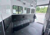Interior of a white horse trailer with padded black walls, barred windows, ceiling lights, and ceiling fans visible.