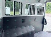 Interior of a horse trailer showing barred stalls, white walls, ceiling fans, and a dark padded lower wall bar.