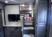 Interior of a dark wood RV with a staircase to a sleeping loft, quilted bed, mounted TV, and built-in cabinets.