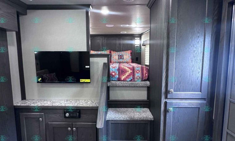 Interior of a dark wood RV with a staircase to a sleeping loft, quilted bed, mounted TV, and built-in cabinets.