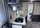 Compact RV kitchen with granite countertop, double sink, and a stove topped by a microwave/hood unit above. Nearby is a doorway to a bathroom.