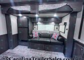 Dark wood RV living area with a black leather sofa, patterned cushions, and overhead cabinets under a corrugated ceiling and recessed lighting.