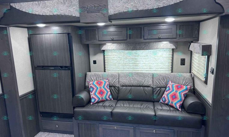 RV living area with dark wood cabinets, gray sofa and colorful geometric pillows, window with blinds, and overhead storage cabinets.