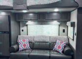 Interior of a dark wood RV with a grey patterned sofa, colorful throw pillows, and overhead cabinets.