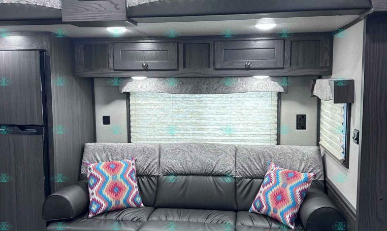 Interior of a dark wood RV with a grey patterned sofa, colorful throw pillows, and overhead cabinets.