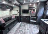 Interior of a dark gray RV living area with a sofa, overhead cabinets, and a TV mounted on the wall.