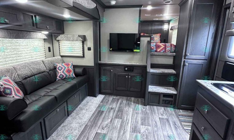 Interior of a dark gray RV living area with a sofa, overhead cabinets, and a TV mounted on the wall.