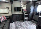 Interior of a dark-wood RV with a couch, TV, cabinets, and stairs; cozy living area on a travel trailer.