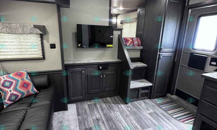 Interior of a dark-wood RV with a couch, TV, cabinets, and stairs; cozy living area on a travel trailer.