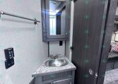 Small bathroom vanity in a dark wood trailer interior with a round sink and mirrored medicine cabinet above it
