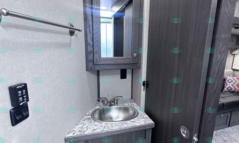 Small bathroom vanity in a dark wood trailer interior with a round sink and mirrored medicine cabinet above it