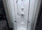 Compact corner shower stall in a trailer bathroom with a white fiberglass enclosure and curved glass doors