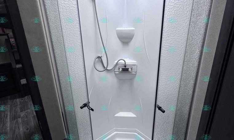 Compact corner shower stall in a trailer bathroom with a white fiberglass enclosure and curved glass doors