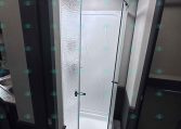 Curved shower enclosure in an RV bathroom with a frosted panel and skylight above.