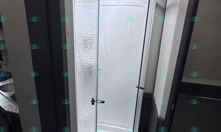 Curved shower enclosure in an RV bathroom with a frosted panel and skylight above.