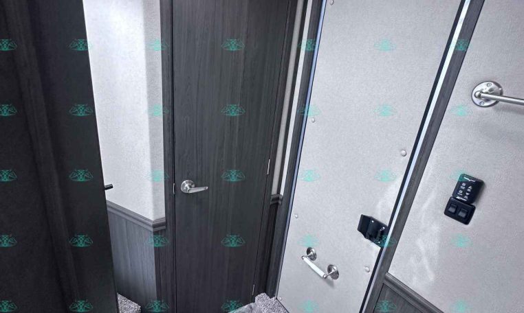 Small bathroom in a trailer with a dark wooden door, light gray walls, and a white toilet in the foreground.