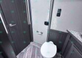 RV bathroom with a white toilet, gray wood-look floor, and dark cabinetry along the walls, plus a towel bar on the right.