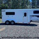 White Shadow Select gooseneck horse trailer with large side window and entry door, parked on gravel with a forest in the background.