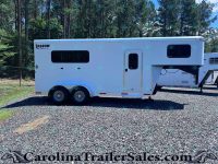 White Shadow Select gooseneck horse trailer with large side window and entry door, parked on gravel with a forest in the background.