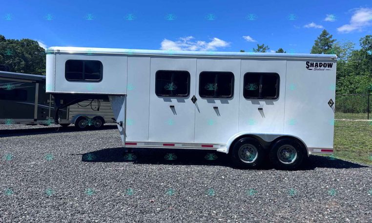 White Shadow Select horse trailer with three side windows, parked on a gravel lot under a clear blue sky.